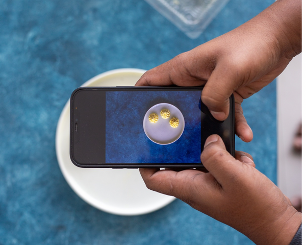 Person using a smartphone to take a photo of a dish on a blue sapphire backdrop